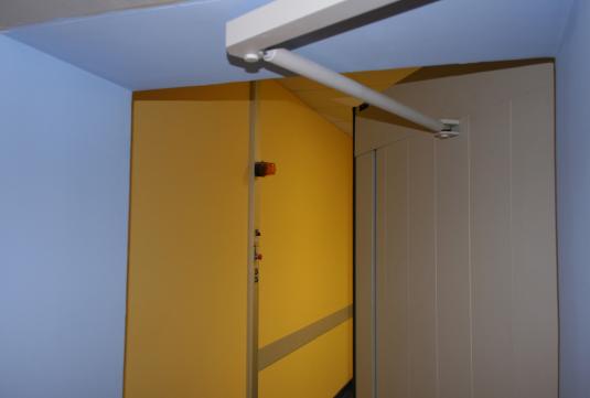 Puerta batiente con brazo de conexión entre la hoja de la puerta y el mecanismo.